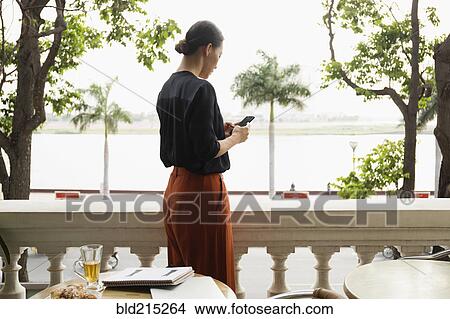 Picture - Asian businesswoman using cell phone on balcony. Fotosearch