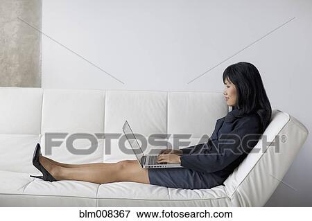 Asian businesswoman with feet up using laptop on sofa View Large Photo Image Stock Photo - Asian businesswoman with feet up using laptop on sofa. Fotosearch