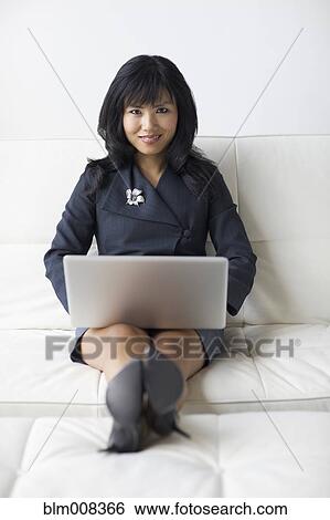 Asian businesswoman with feet up using laptop on sofa View Large Photo Image Stock Photograph - Asian businesswoman with feet up using laptop on sofa. Fotosearch