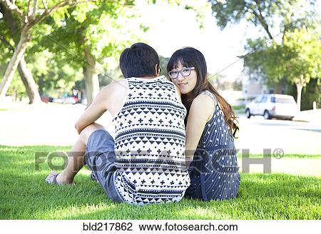 Stock Image - Asian couple sitting in park. Fotosearch