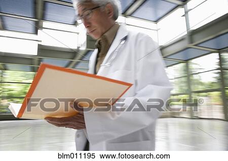 Stock Photography - Asian doctor walking and looking at medical record. Fotosearch