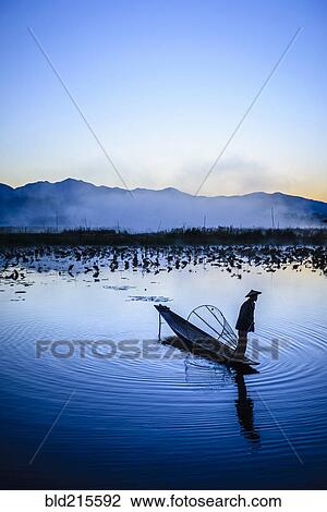 Stock Image - Asian fisherman using fishing net in canoe on river. Fotosearch