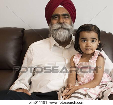 Stock Image - Asian grandfather sitting on sofa with granddaughter. Fotosearch