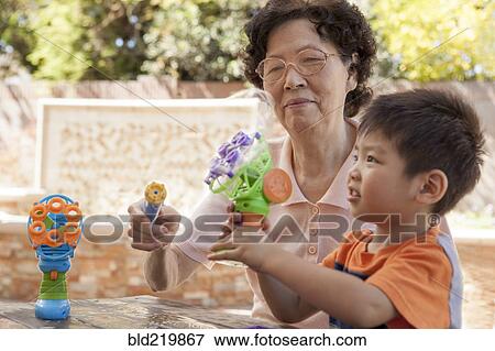 Stock Photo - Asian grandmother and grandson blowing bubbles outdoors. Fotosearch