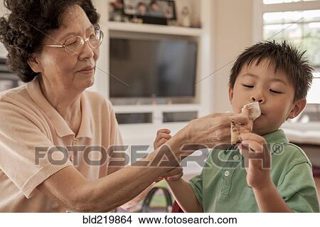 Picture - Asian grandmother wiping face of grandson at table. Fotosearch