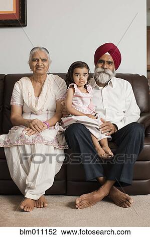 Stock Image - Asian grandparents sitting on sofa with granddaughter. Fotosearch