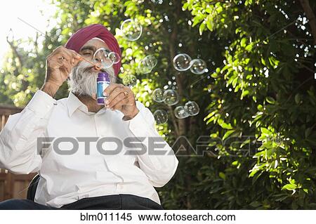Stock Photography - Asian man blowing bubbles outdoors. Fotosearch