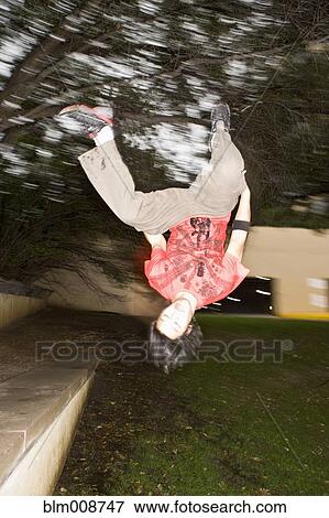 Stock Photo - Asian man jumping upside-down in park. Fotosearch