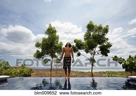 Stock Image - Asian man standing on edge of infinity swimming pool. Fotosearch