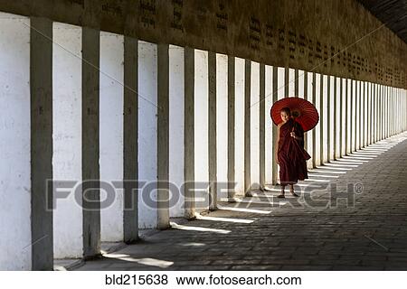 Stock Photo - Asian monk-in-training carrying parasol in hallway. Fotosearch
