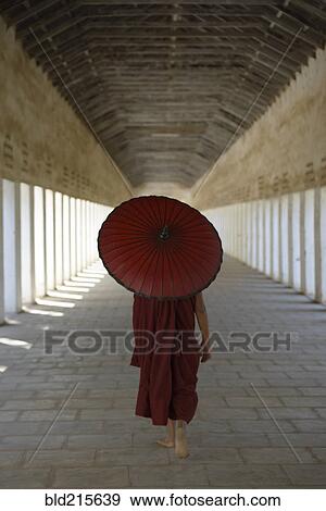 Stock Photo - Asian monk-in-training carrying parasol in hallway. Fotosearch