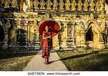 Picture - Asian monk-in-training holding parasol outside ornate temple. Fotosearch