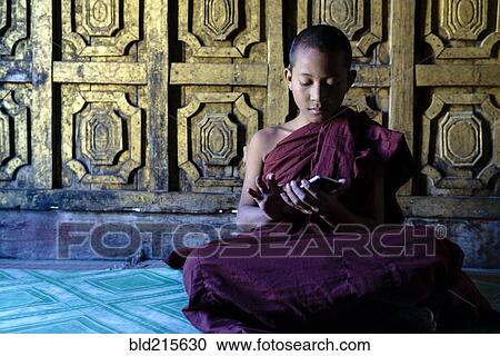 Stock Image - Asian monk-in-training using cell phone in temple. Fotosearch