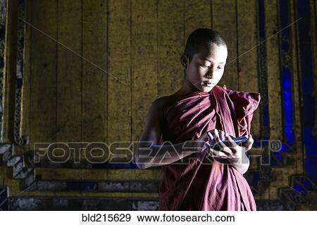 Stock Photo - Asian monk-in-training using cell phone in temple. Fotosearch