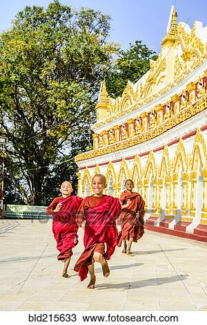 Stock Image - Asian monks-in-training running outside ornate temple. Fotosearch