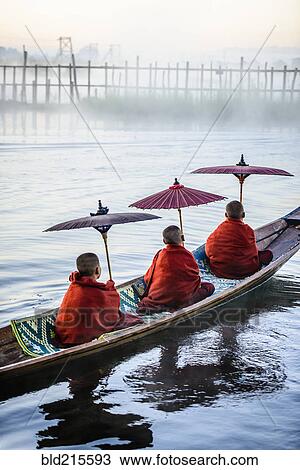 Stock Image - Asian monks under parasols in canoe on river. Fotosearch