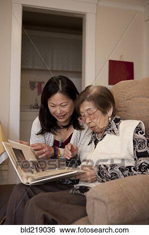 Stock Photograph - Asian mother and daughter looking at photo album. Fotosearch