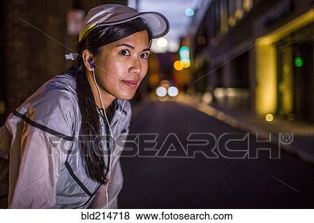 Stock Photo - Asian runner resting on city street at night. Fotosearch
