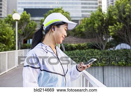 Stock Photo - Asian runner using cell phone in city. Fotosearch