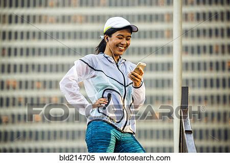 Stock Photography - Asian runner using cell phone near highrise building. Fotosearch