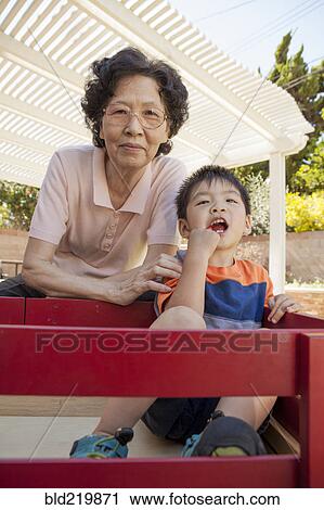 Stock Image - Asian woman and grandson relaxing in backyard. Fotosearch