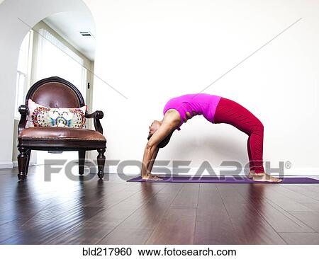 Stock Image - Asian woman practicing yoga in living room. Fotosearch