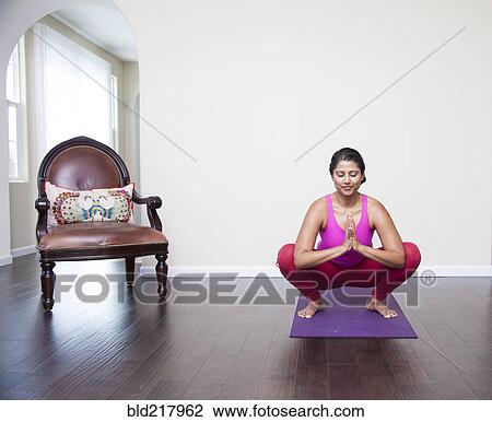 Stock Image - Asian woman practicing yoga in living room. Fotosearch