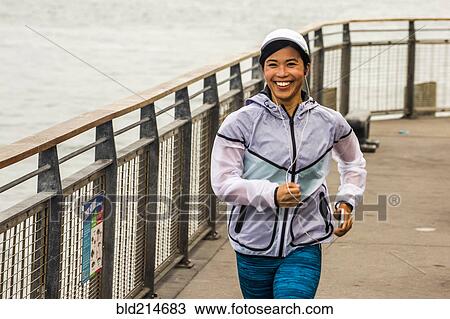 Stock Image - Asian woman running at waterfront. Fotosearch