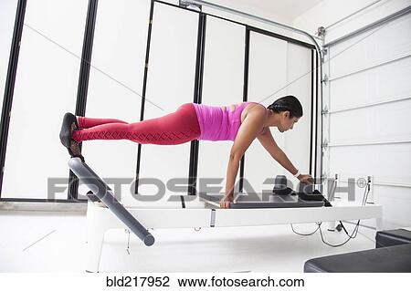 Stock Image - Asian woman using exercise machine in gymnasium. Fotosearch
