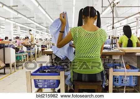 Stock Image - Asian worker sewing clothing in garment factory. Fotosearch