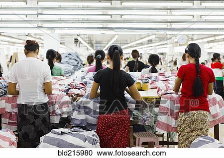 Stock Image - Asian workers sewing clothing in garment factory. Fotosearch