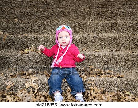 Stock Photograph - Baby girl sitting in autumn leaves on front steps. Fotosearch