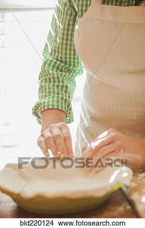 Picture - Baker pressing pie dough in dish. Fotosearch