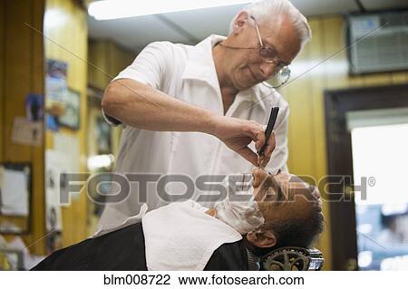 Stock Image - Barber giving customer old-fashioned shave in barbershop. Fotosearch