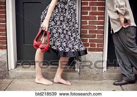 Stock Photo - Barefoot girl holding shoes near boyfriend in doorway. Fotosearch