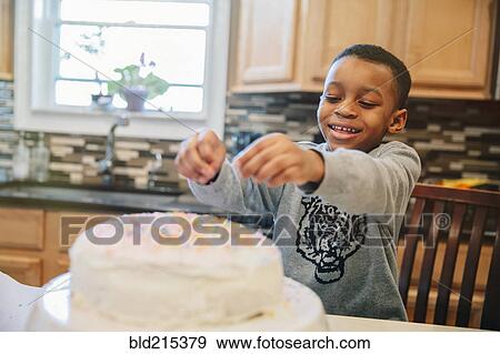 Stock Photo - Black boy decorating cake in kitchen. Fotosearch