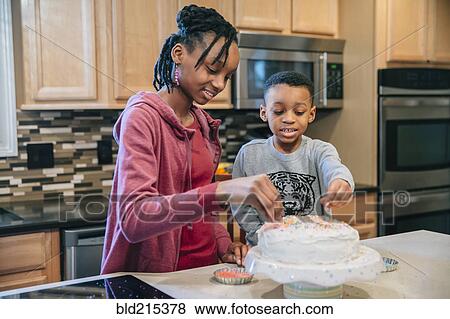 Stock Photo - Black brother and sister decorating cake in kitchen. Fotosearch