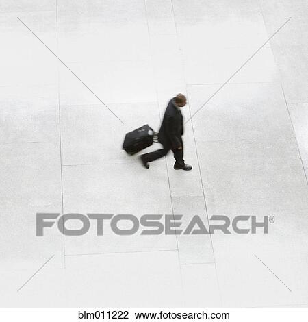 Stock Image - Black businessman pulling suitcase through lobby. Fotosearch