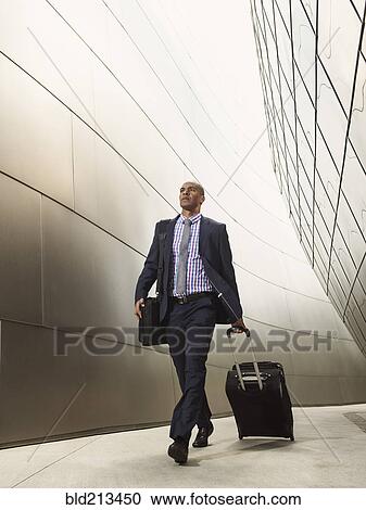 Stock Image - Black businessman rolling luggage. Fotosearch