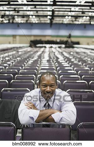 Stock Image - Black businessman sitting in empty conference center. Fotosearch