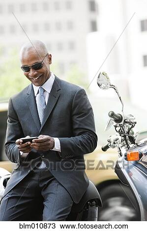 Stock Image - Black businessman sitting on scooter text messaging. Fotosearch