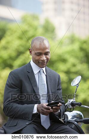 Stock Photograph - Black businessman sitting on scooter text messaging. Fotosearch