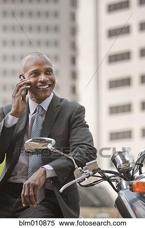 Stock Photography - Black businessman sitting on scooter talking on cell phone. Fotosearch