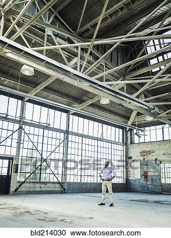 Stock Image - Black businessman standing in empty warehouse. Fotosearch
