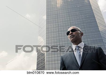 Stock Image - Black businessman standing near highrise. Fotosearch