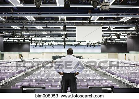 Stock Image - Black businessman standing on stage in empty conference center. Fotosearch