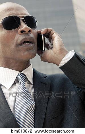 Stock Image - Black businessman talking on cell phone outdoors. Fotosearch