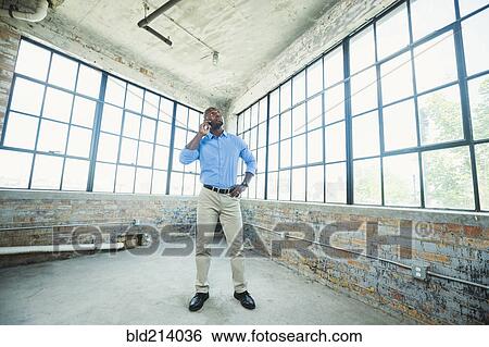 Stock Photograph - Black businessman talking on cell phone in warehouse. Fotosearch