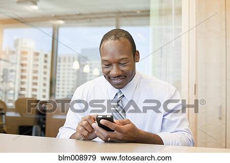 Stock Photo - Black businessman text messaging in office. Fotosearch