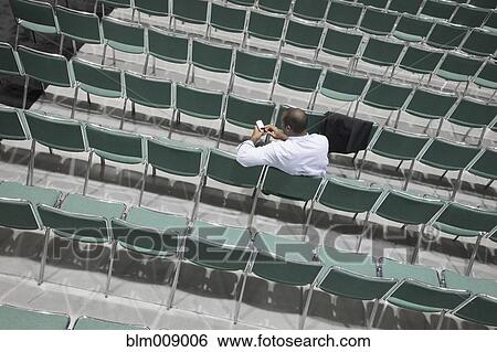 Stock Photograph - Black businessman text messaging in empty conference center. Fotosearch